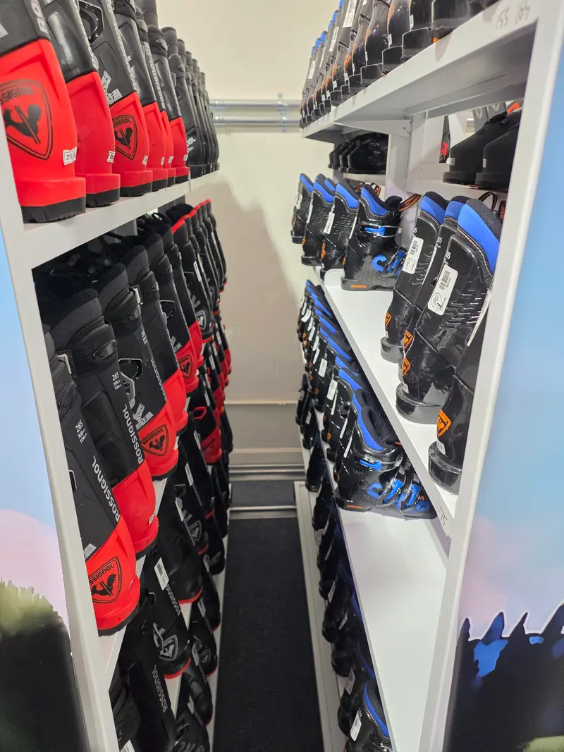 Red and black Rossignol ski boots and blue and black ski boots on white shelves