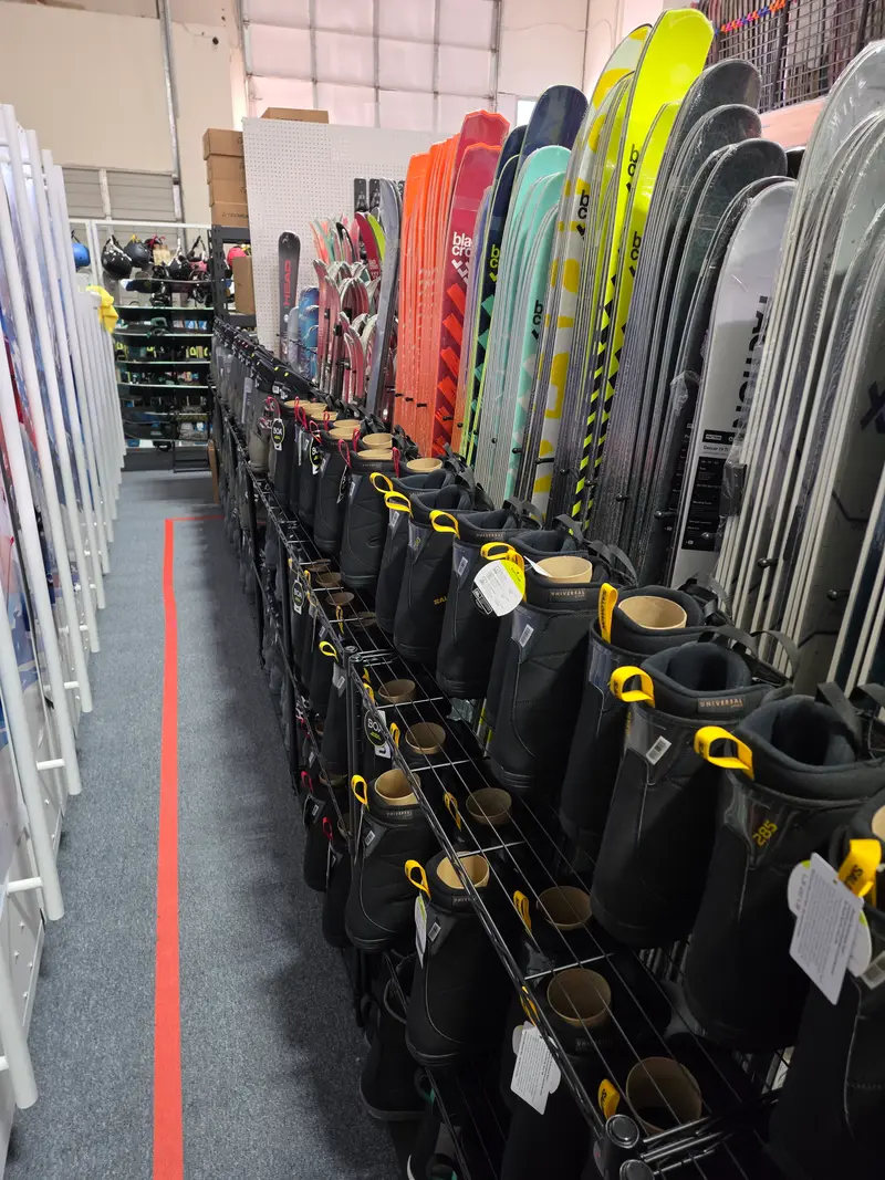 Rows of snowboard boots, including Salomon boots with BOA dials, in front of Black Crows, Faction and Head skis